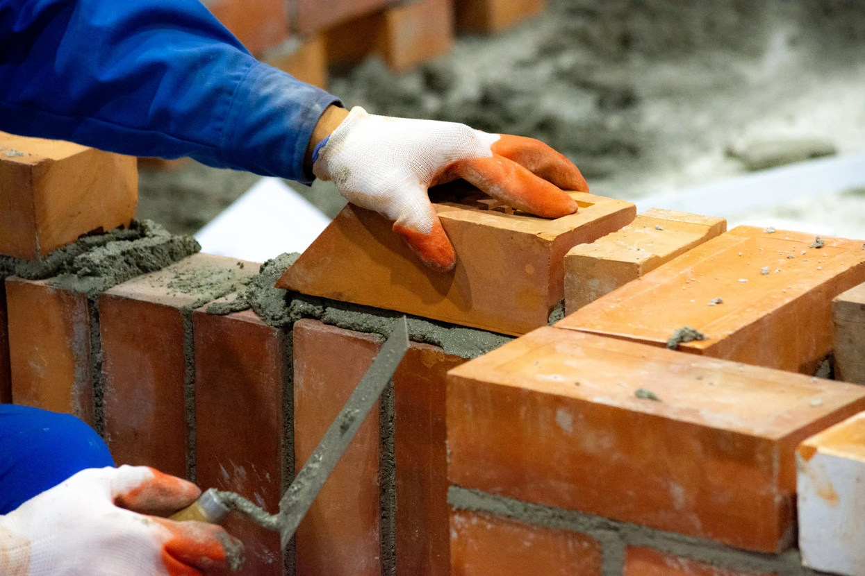 Chantier de construction en extérieur avec maçon posant des briques rouges