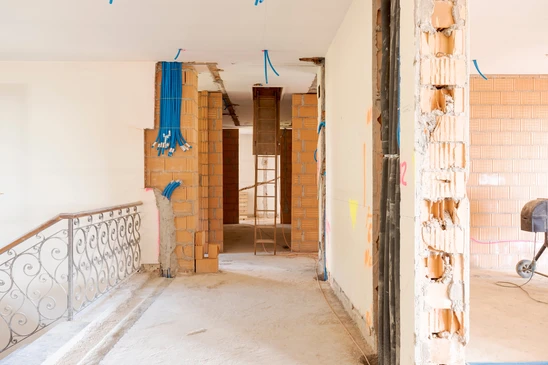 Chantier de rénovation intérieure avec murs en briques creuses apparentes, câbles électriques bleus en attente, escalier avec rampe en fer forgé décorative