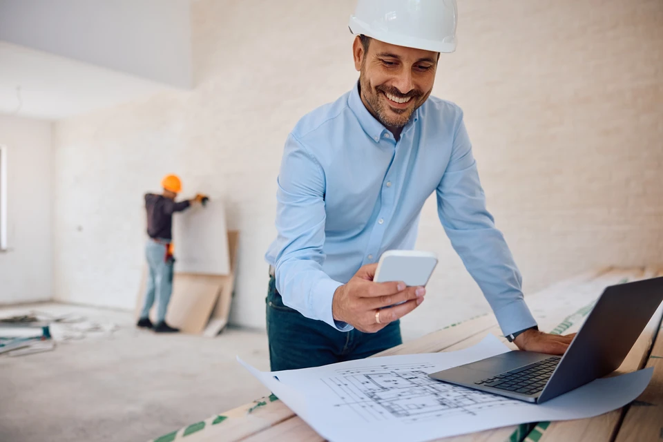 Ouvrier du bâtiment en casque de sécurité jaune consulte une tablette numérique sur chantier de construction