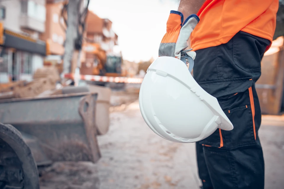 Chantier de construction extérieur avec ingénieur en casque jaune et gilet haute visibilité consultant des plans architecturaux sur table de chantier
